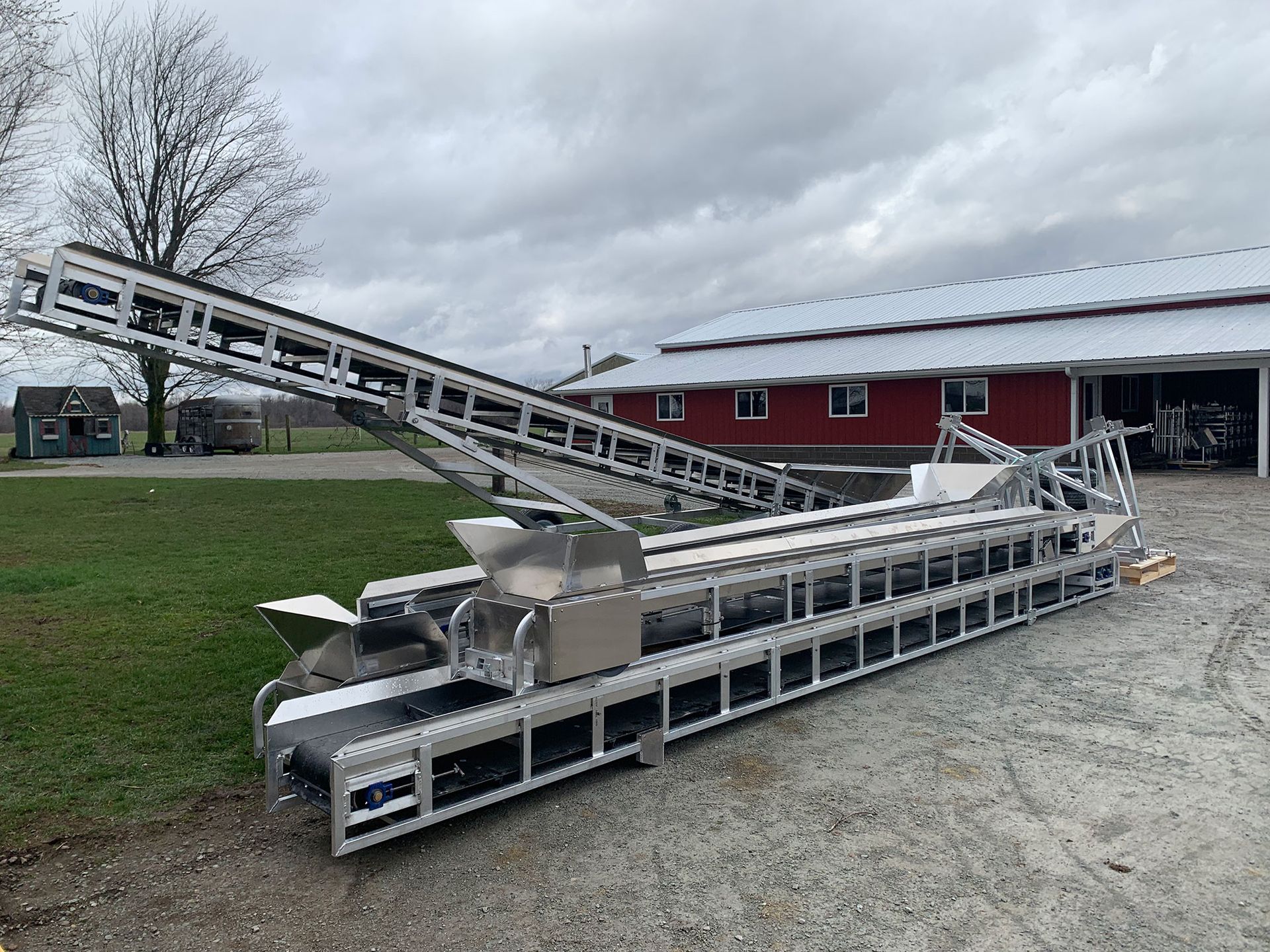 A conveyor belt is sitting in front of a red barn.