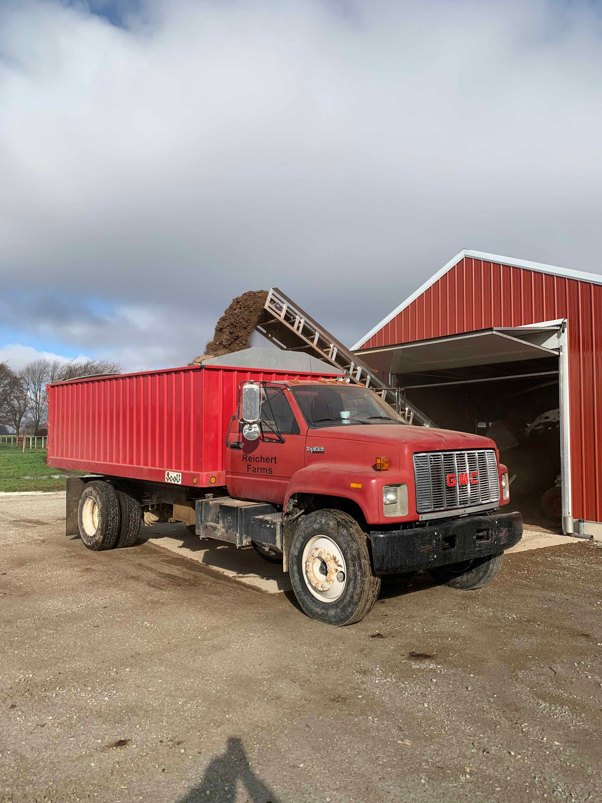 A red dump truck is parked in front of a red barn.