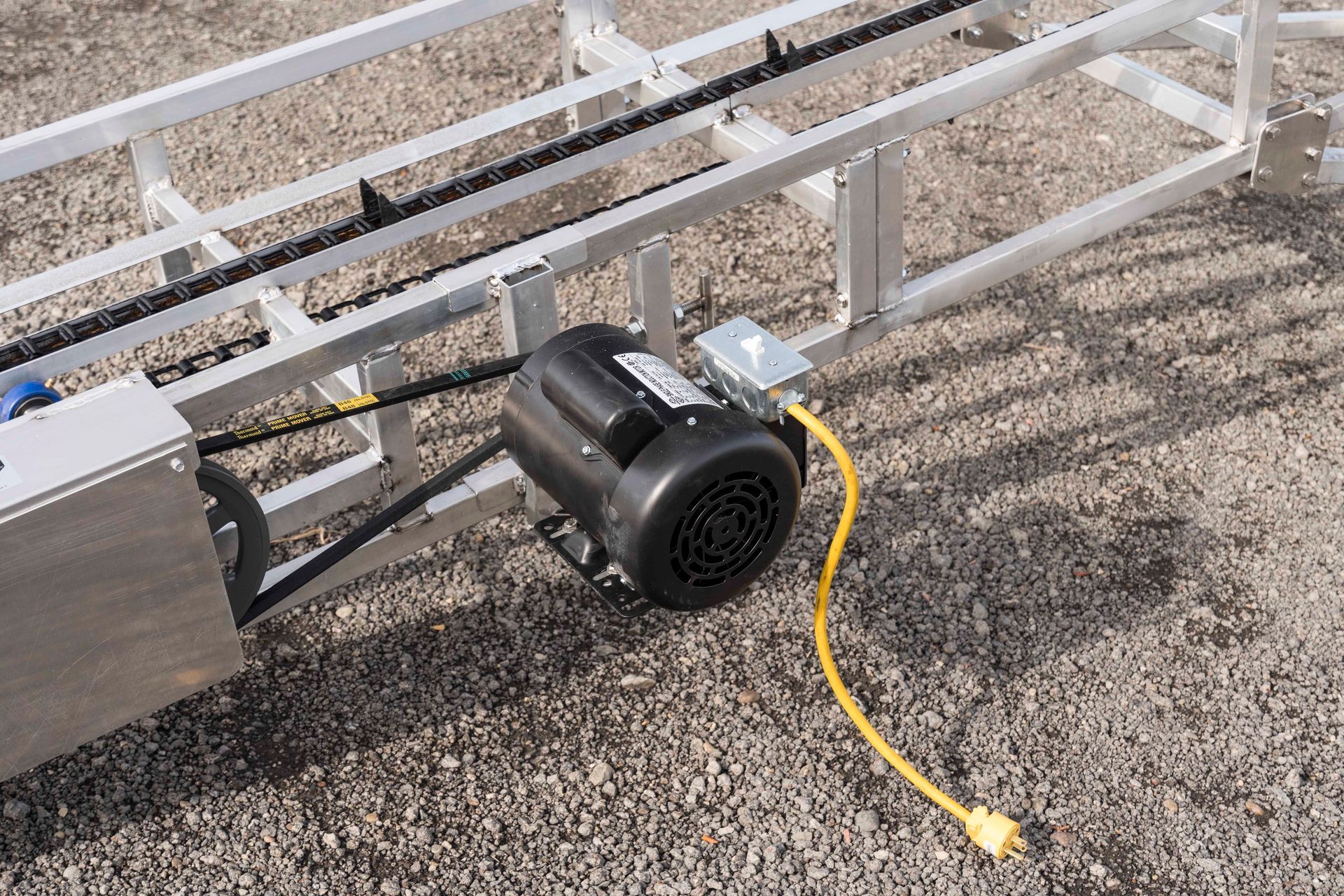 A motor with a yellow cord attached to it is sitting on the ground.