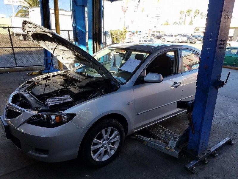 Silver car on a lift with the hood open in an auto repair shop.