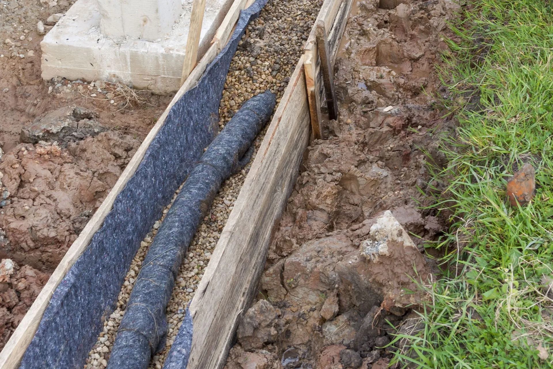 Drainage system construction: black corrugated pipe in trench lined with gravel and fabric.