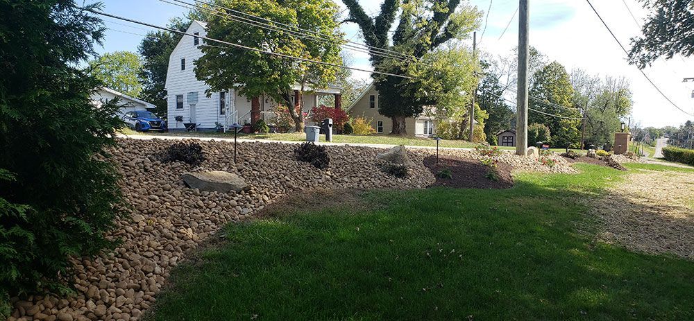 A grassy landscape with a stone wall and houses in the background under a blue sky.