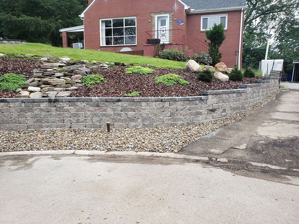 Brick house with landscaping featuring a retaining wall, plants, and small rocks.