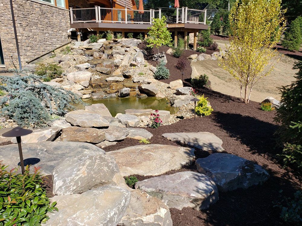 Rocky waterfall feature with a pond in a landscaped yard.