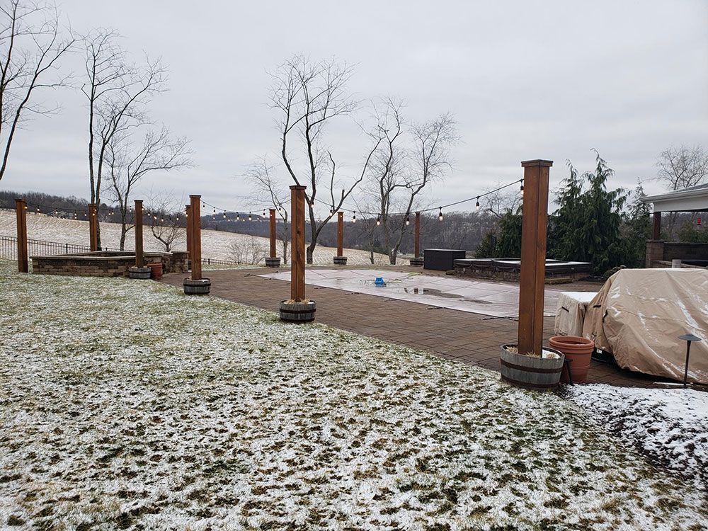Snowy backyard with wooden posts, string lights, and a partially covered pool. Hills in the background.