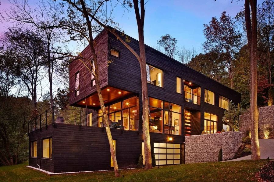 Modern black house with large windows, built into a hillside, trees surrounding.