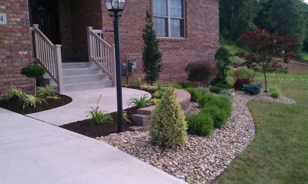 Landscaped front yard with shrubs, rocks, walkway, stairs, and a lamppost.