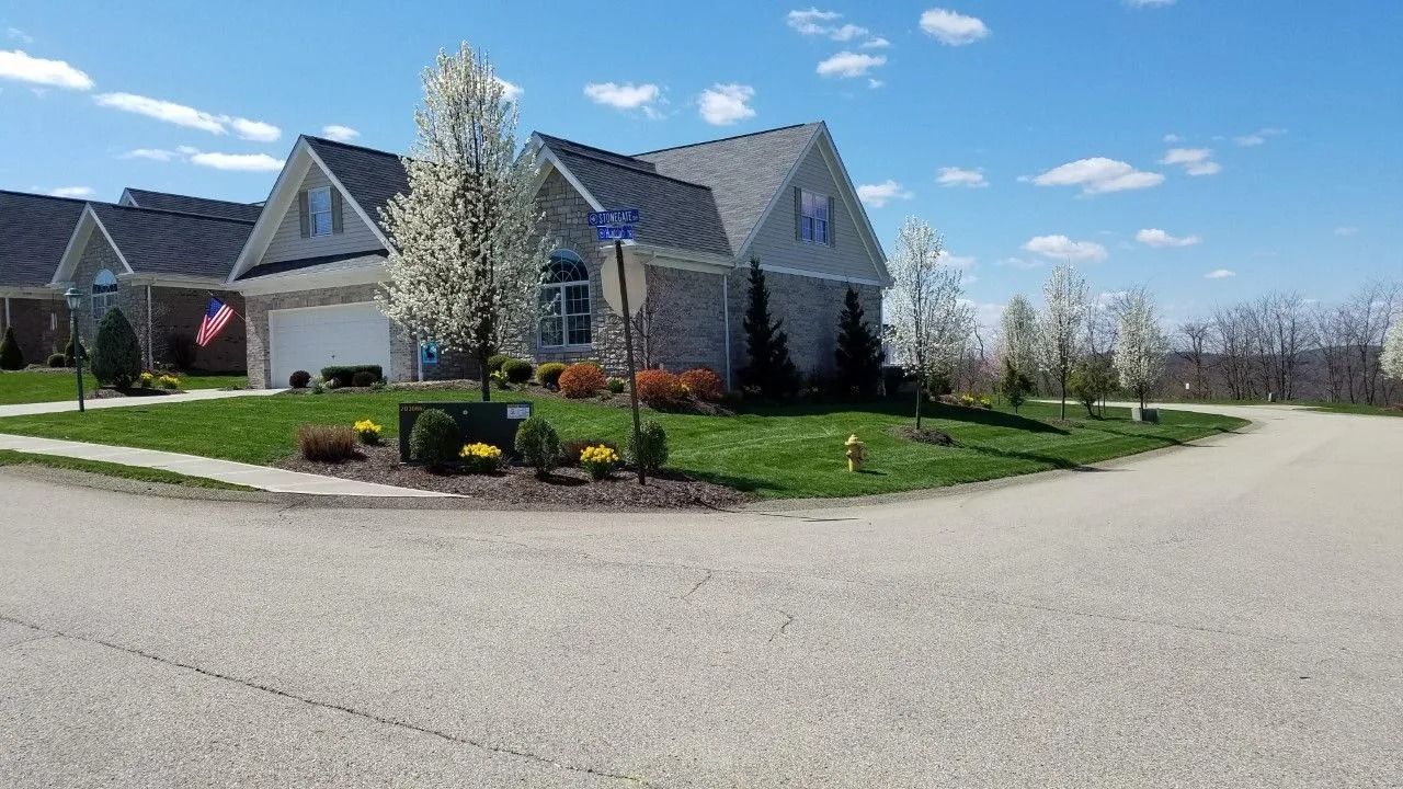 Suburban house with gray roof, green lawn, blooming trees, and blue sky.