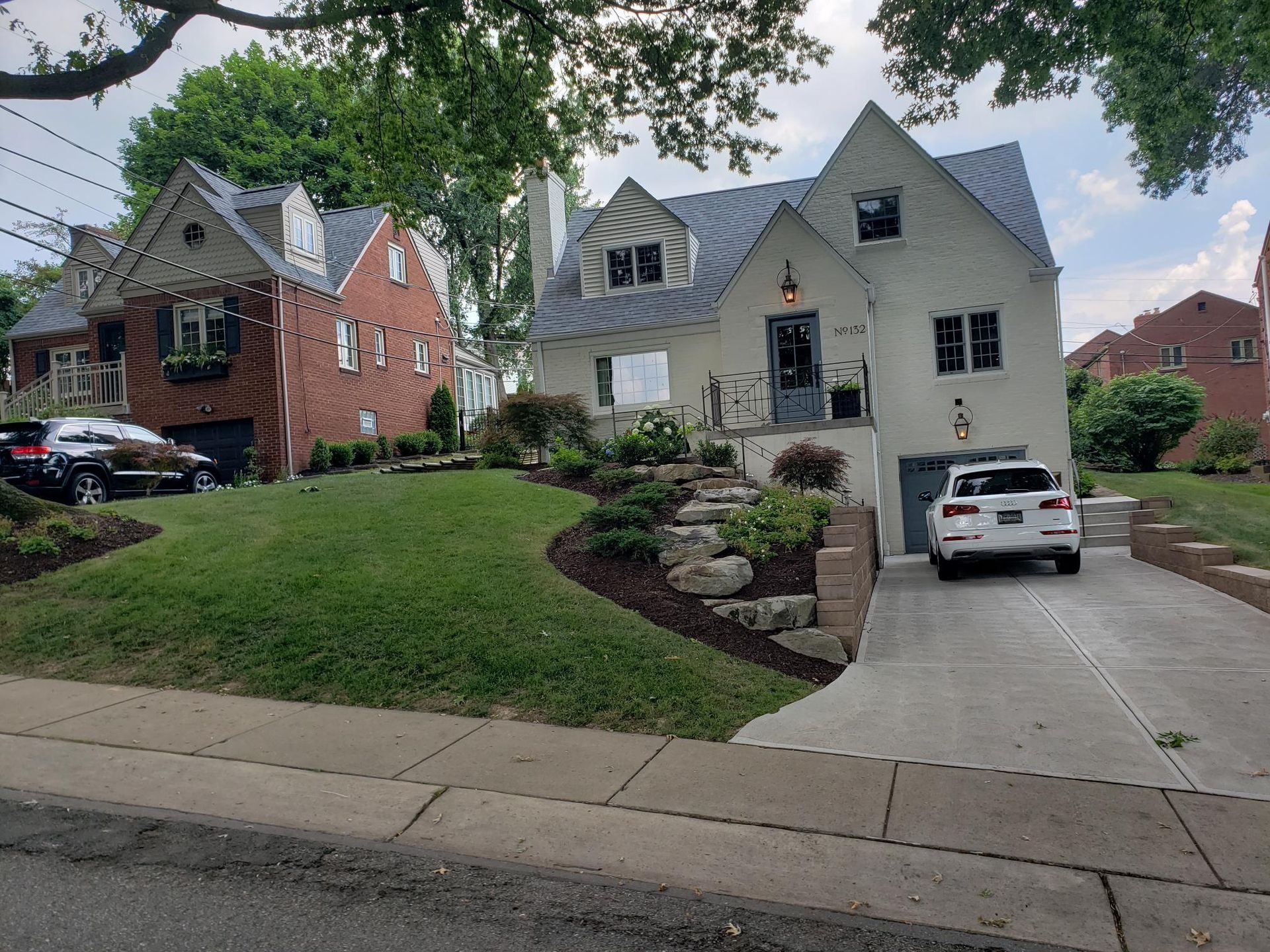 Two houses with manicured lawns and landscaping. A car sits in each driveway.