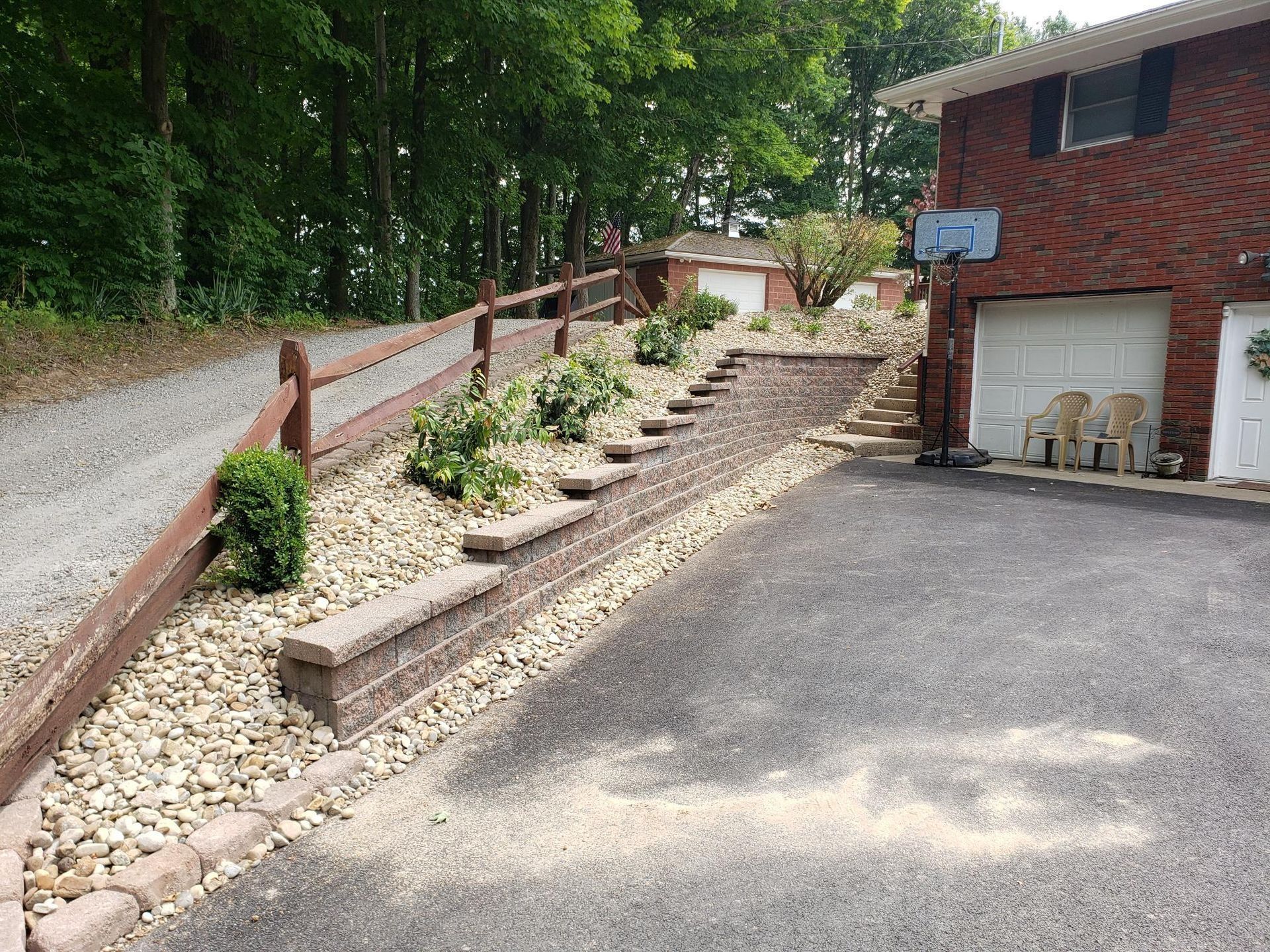 Brick house with gravel driveway, retaining wall with steps, and wooden fence.