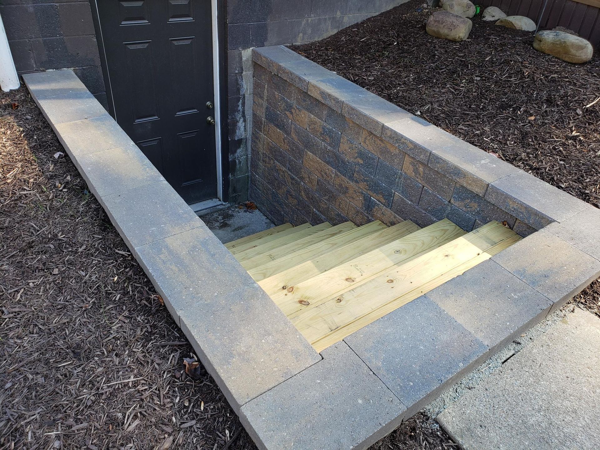 Stone staircase leading down to a basement door, surrounded by a stone and brick wall.