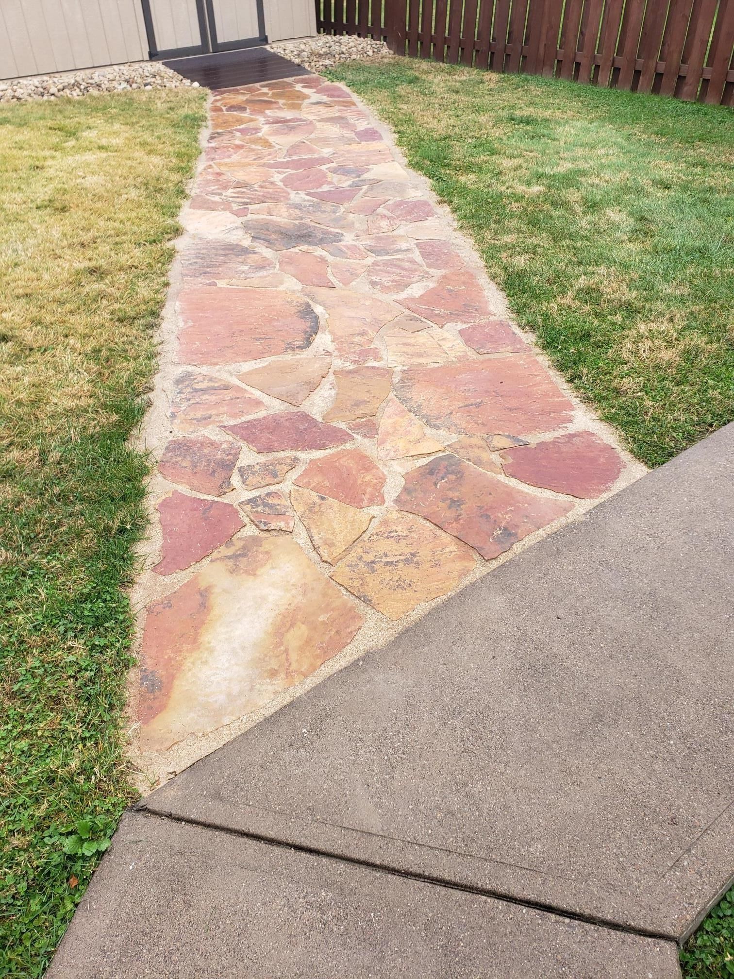 Stone path through grass leading to a gate, intersecting a concrete sidewalk.