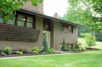Brick house with brown trim and a well-manicured lawn. Landscaping includes bushes and small trees.