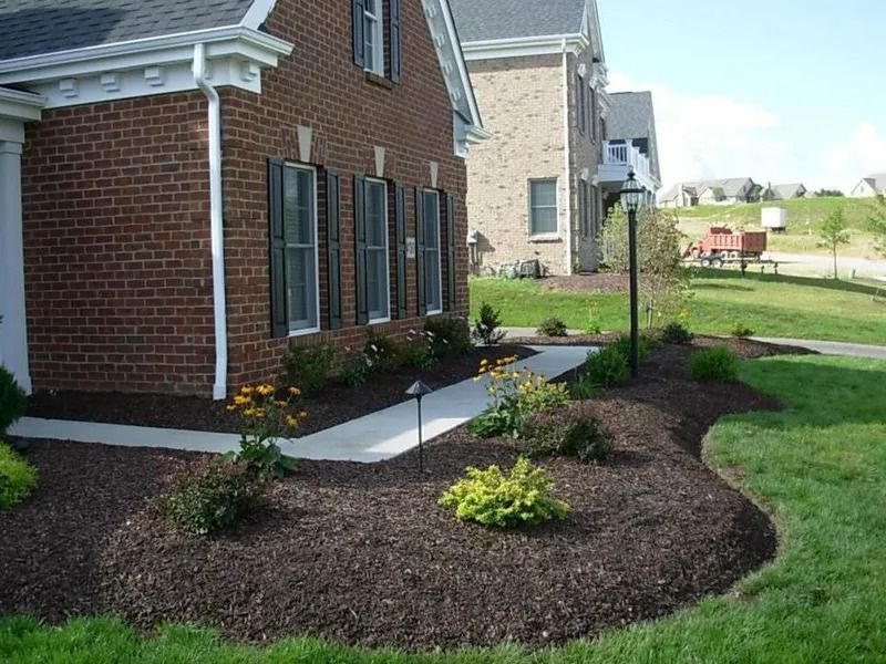 Brick house with a landscaped front yard; dark mulch, concrete walkway, and green grass.