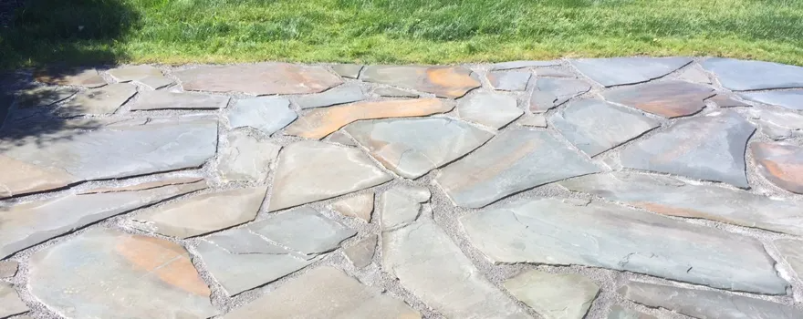 Stone patio with green grass in the background. The stones are various shades of gray and tan.