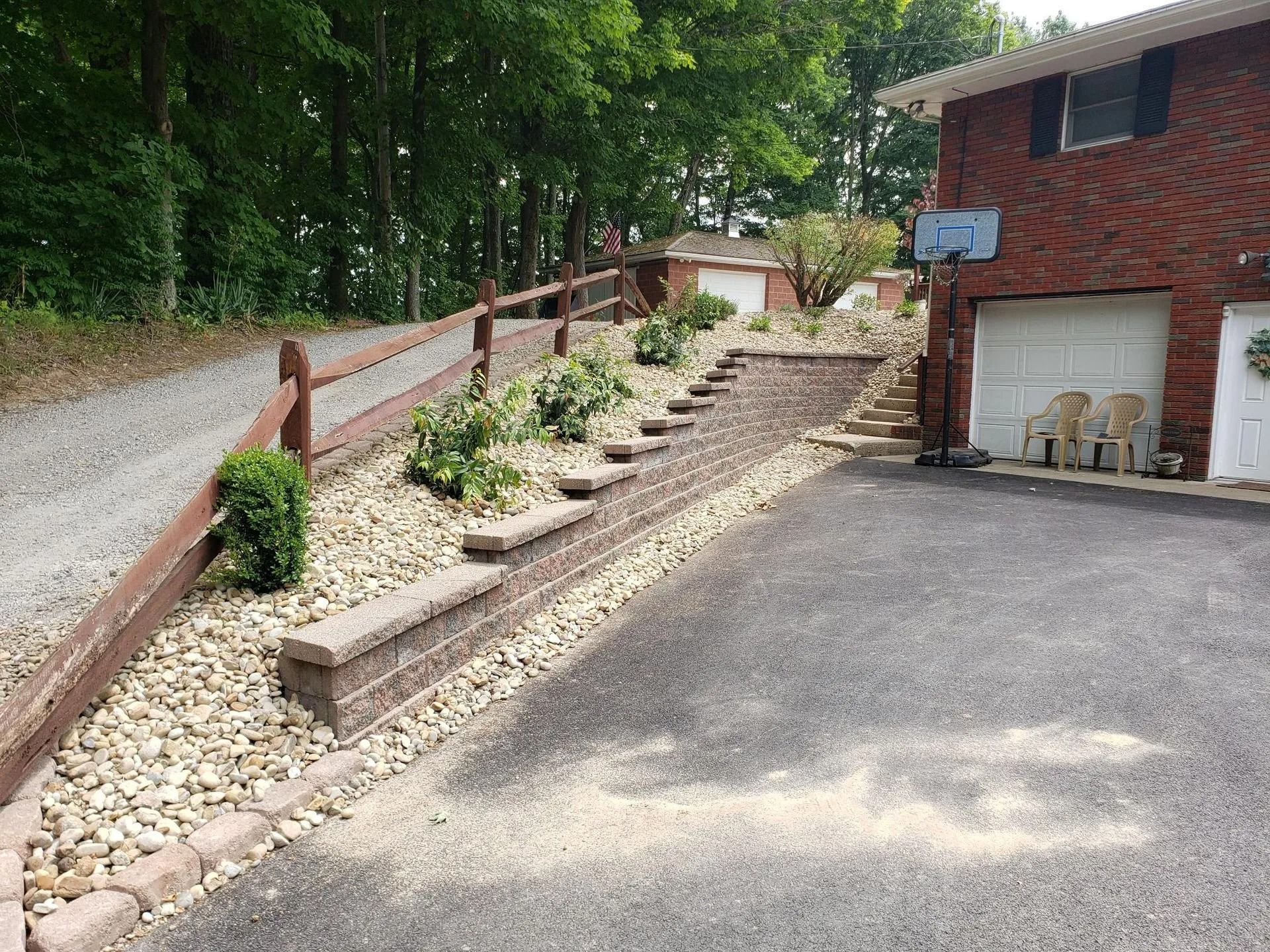 Driveway with retaining wall and landscaping leading to a house with a basketball hoop.