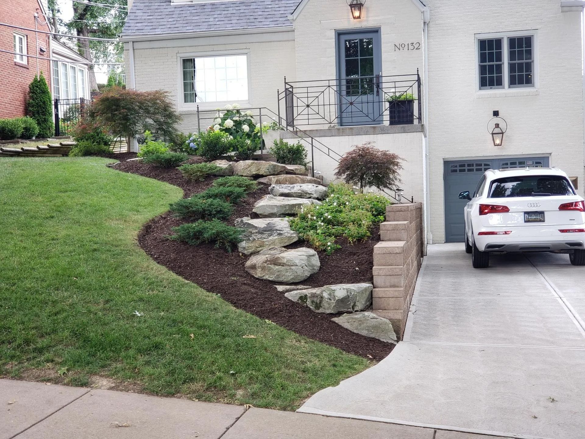 House exterior with landscaping and stone steps. White vehicle parked in driveway.