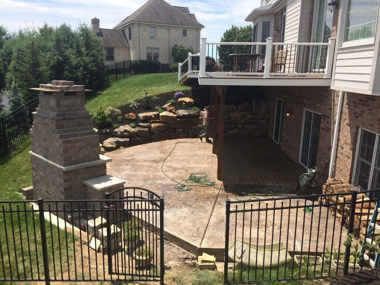 Backyard patio with fireplace, overlooking a sloped lawn, retaining wall, and two-story house.