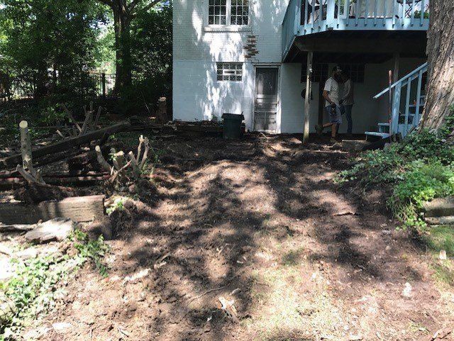 Backyard with excavated dirt path leading to a white house with a person standing on a blue deck.