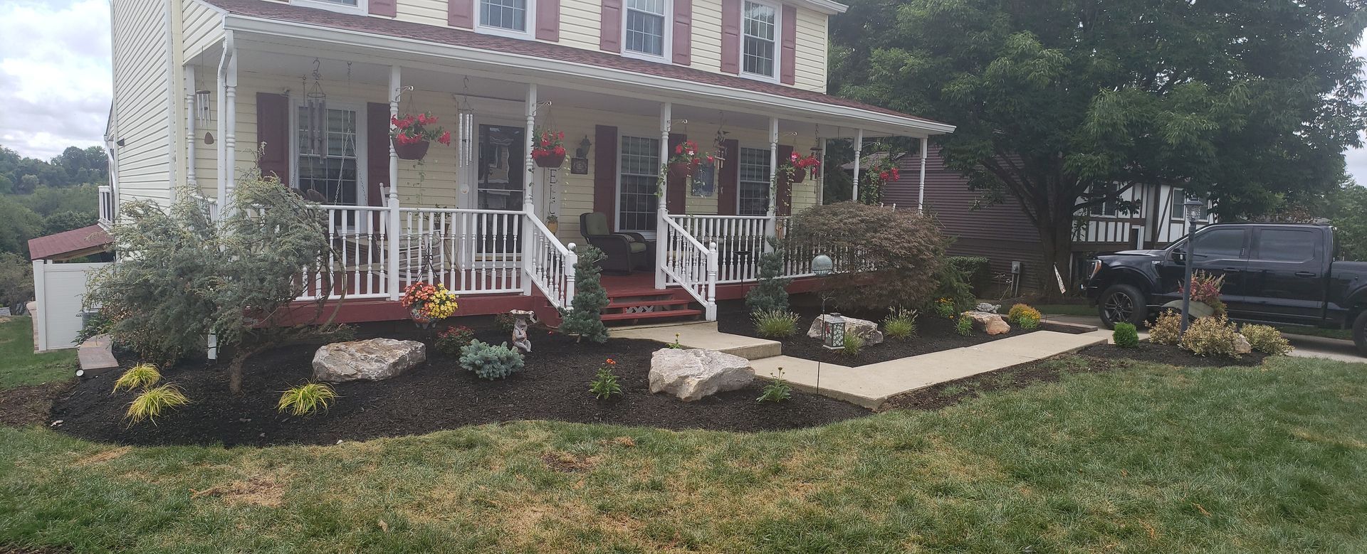 Landscaped front yard with dark green house; flower bed with rocks and colorful bushes.
