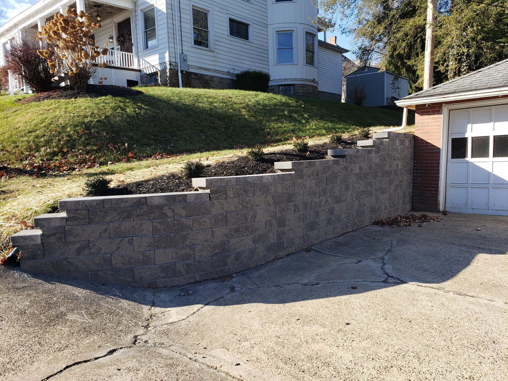 Stone retaining wall with lush green lawn, containing green bushes and red flowers.