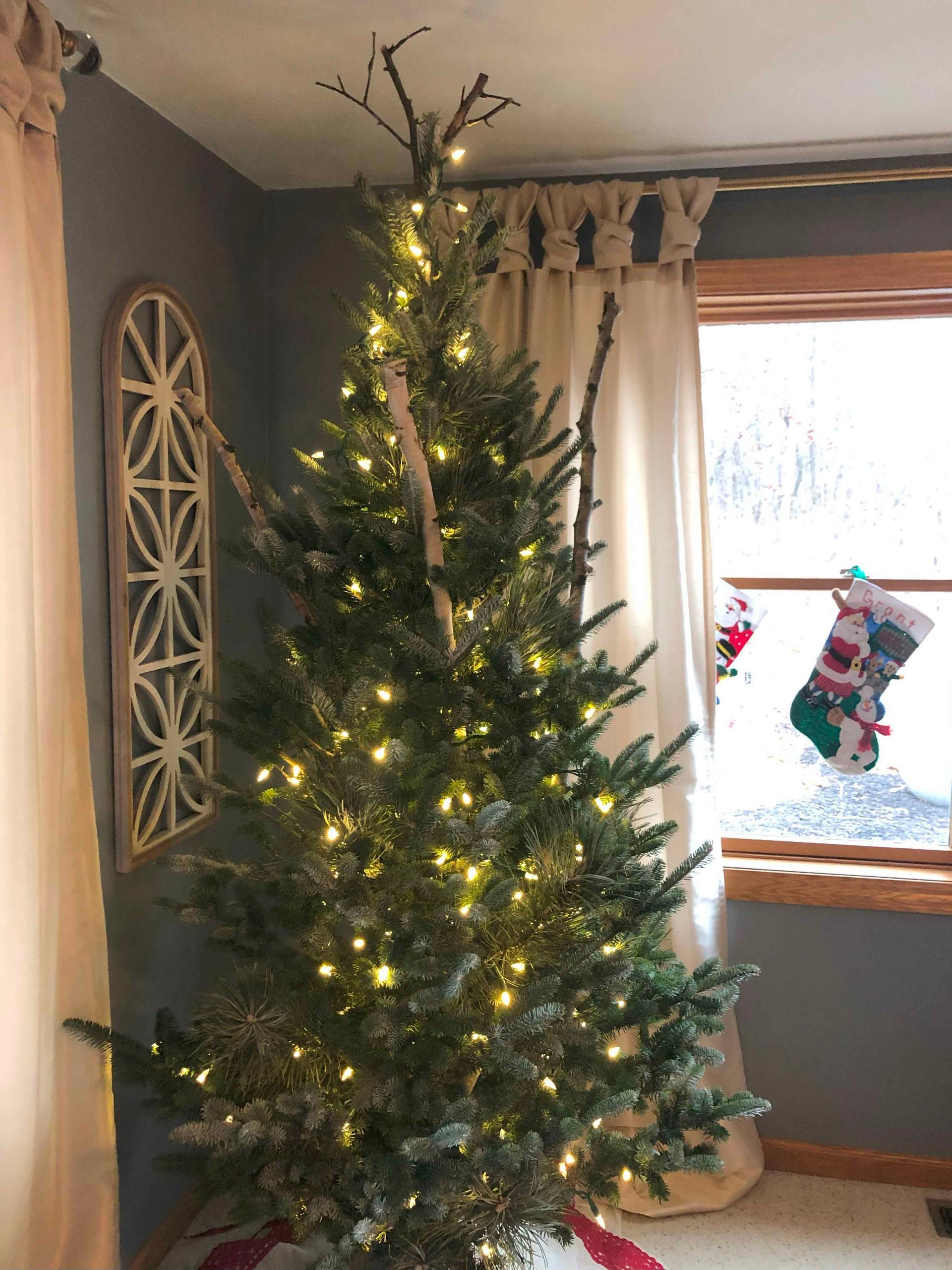 A christmas tree is sitting in a living room next to a window.