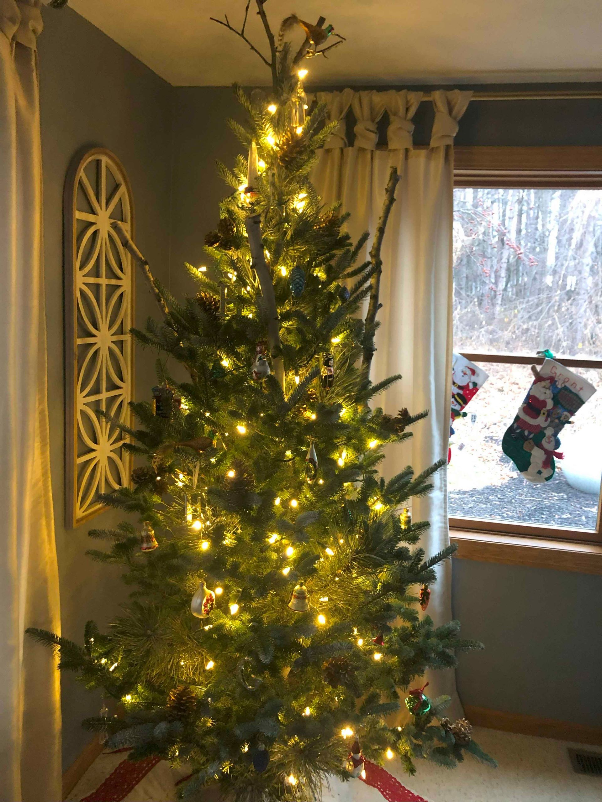 A christmas tree is lit up in a living room next to a window.