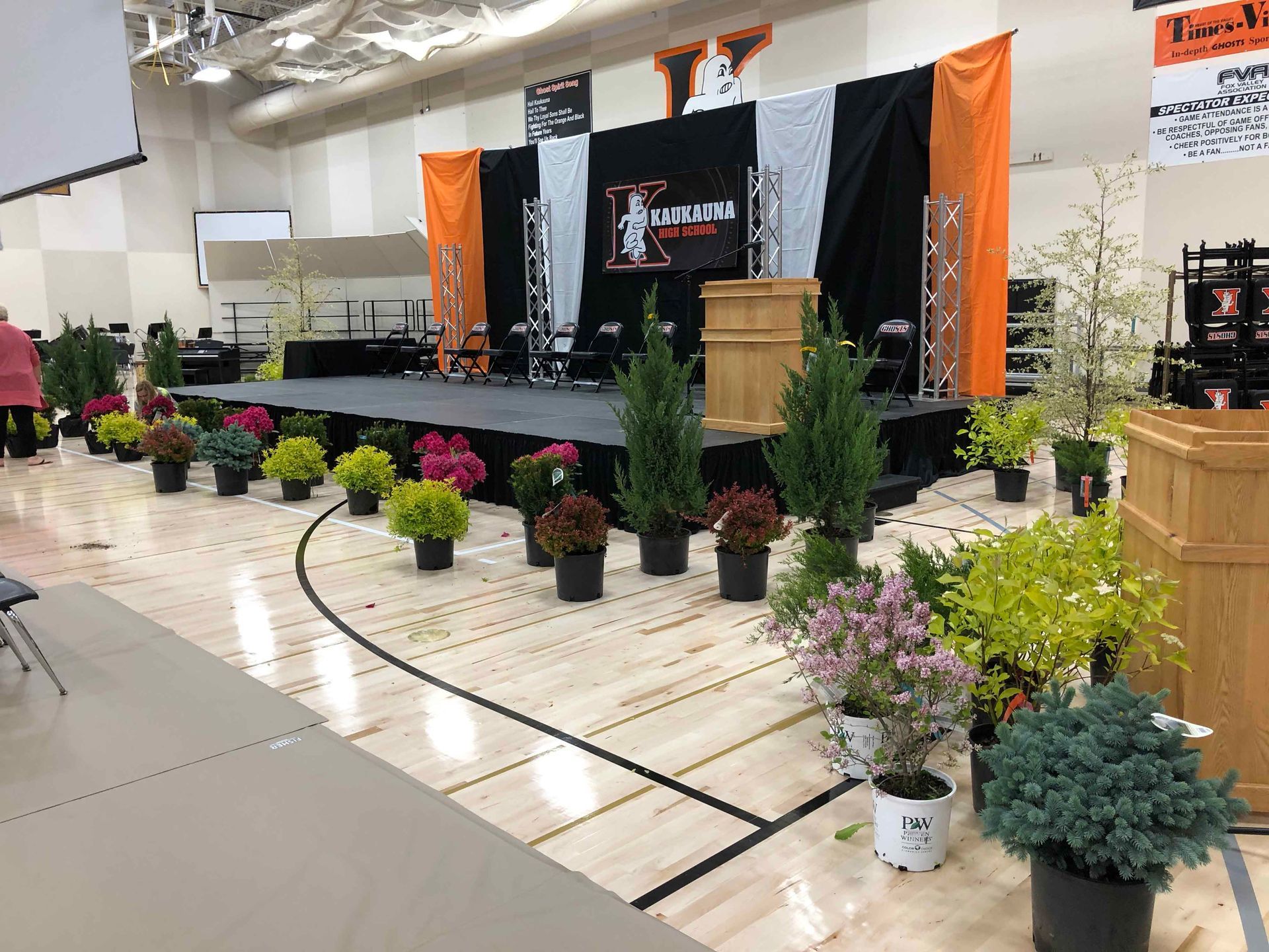 A gym filled with potted plants and a stage.