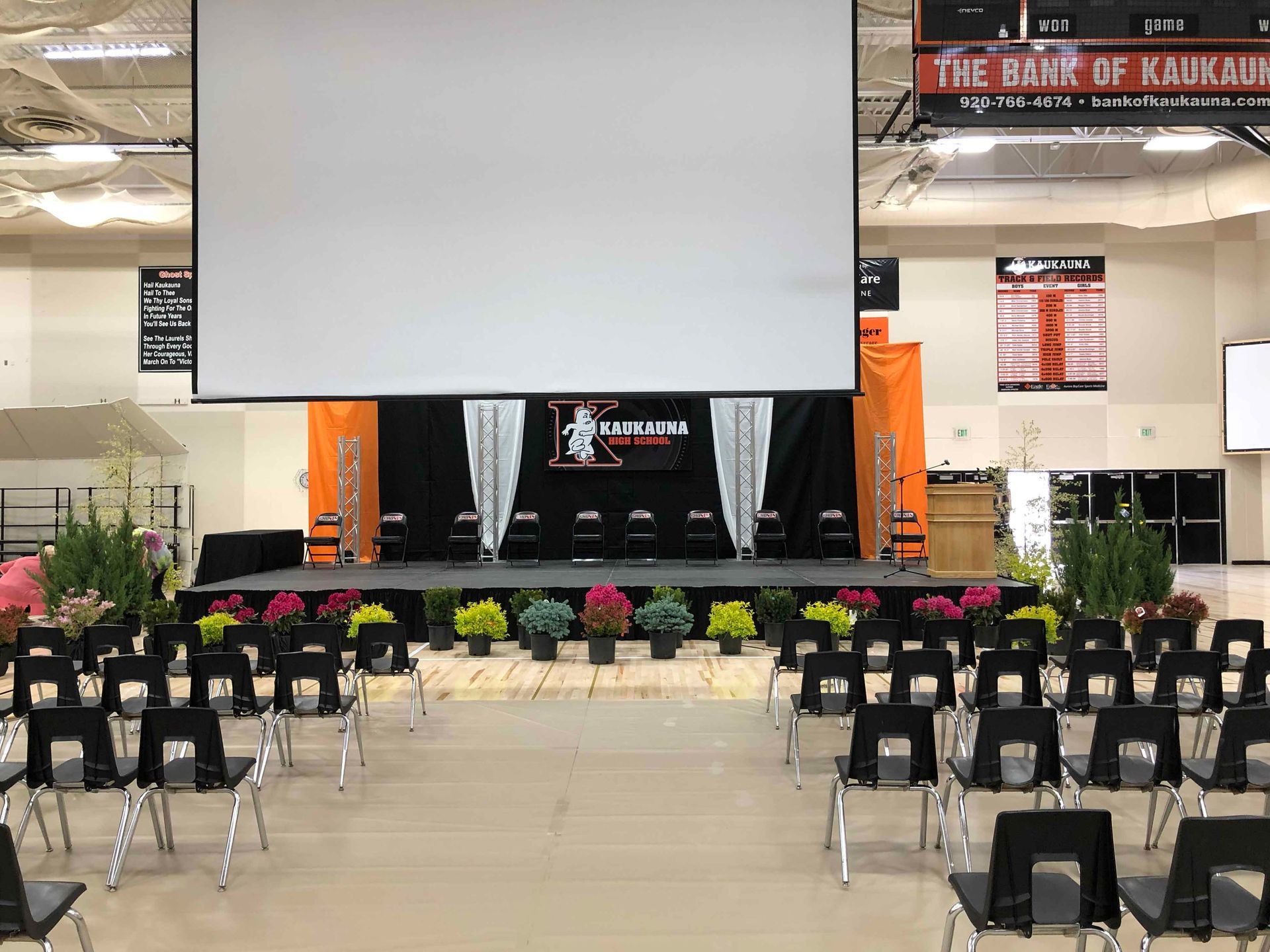 A large room with a stage and chairs and a projector screen.