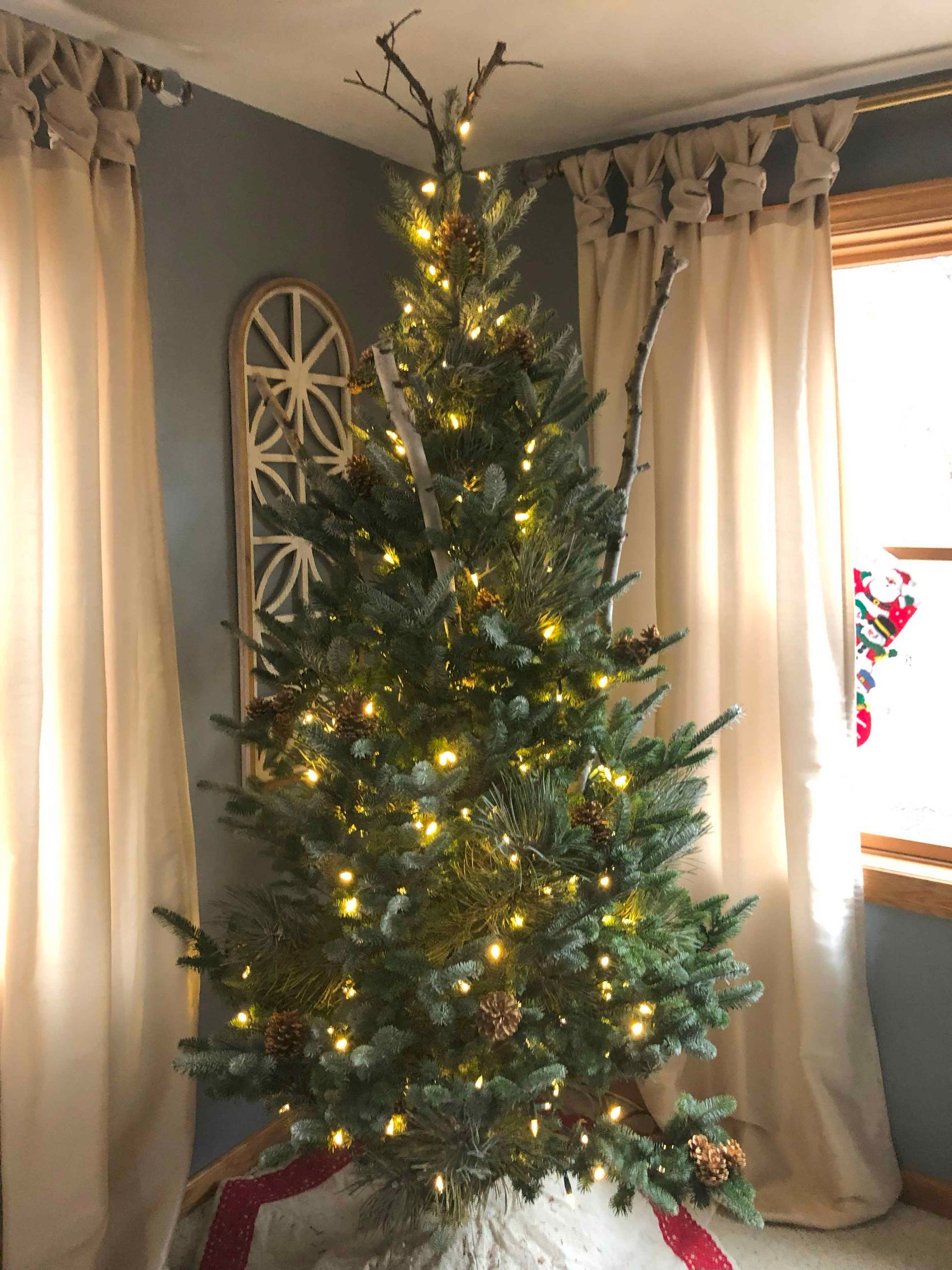 A christmas tree is sitting in a living room next to a window.