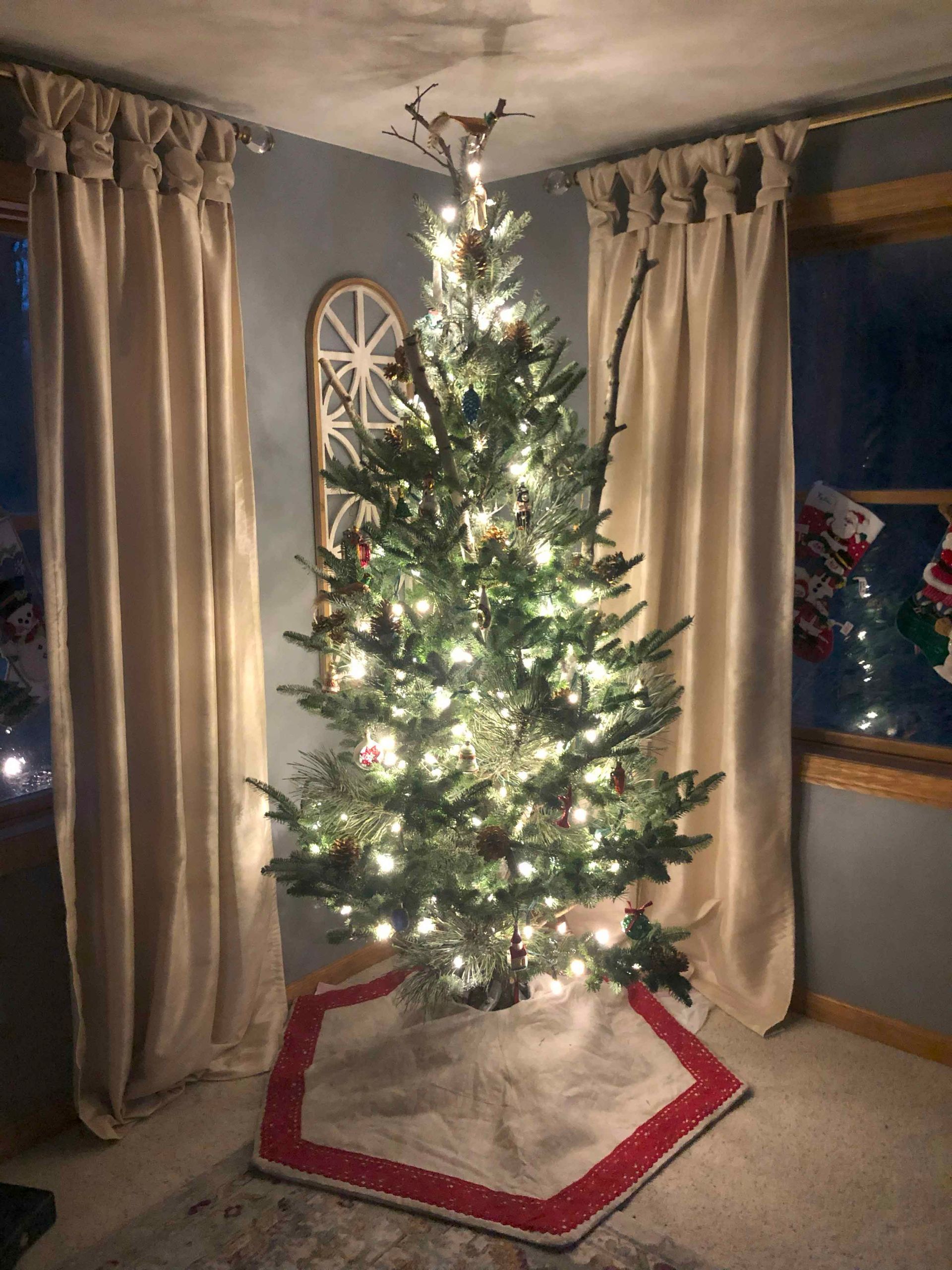 A christmas tree is sitting in a living room next to a window.