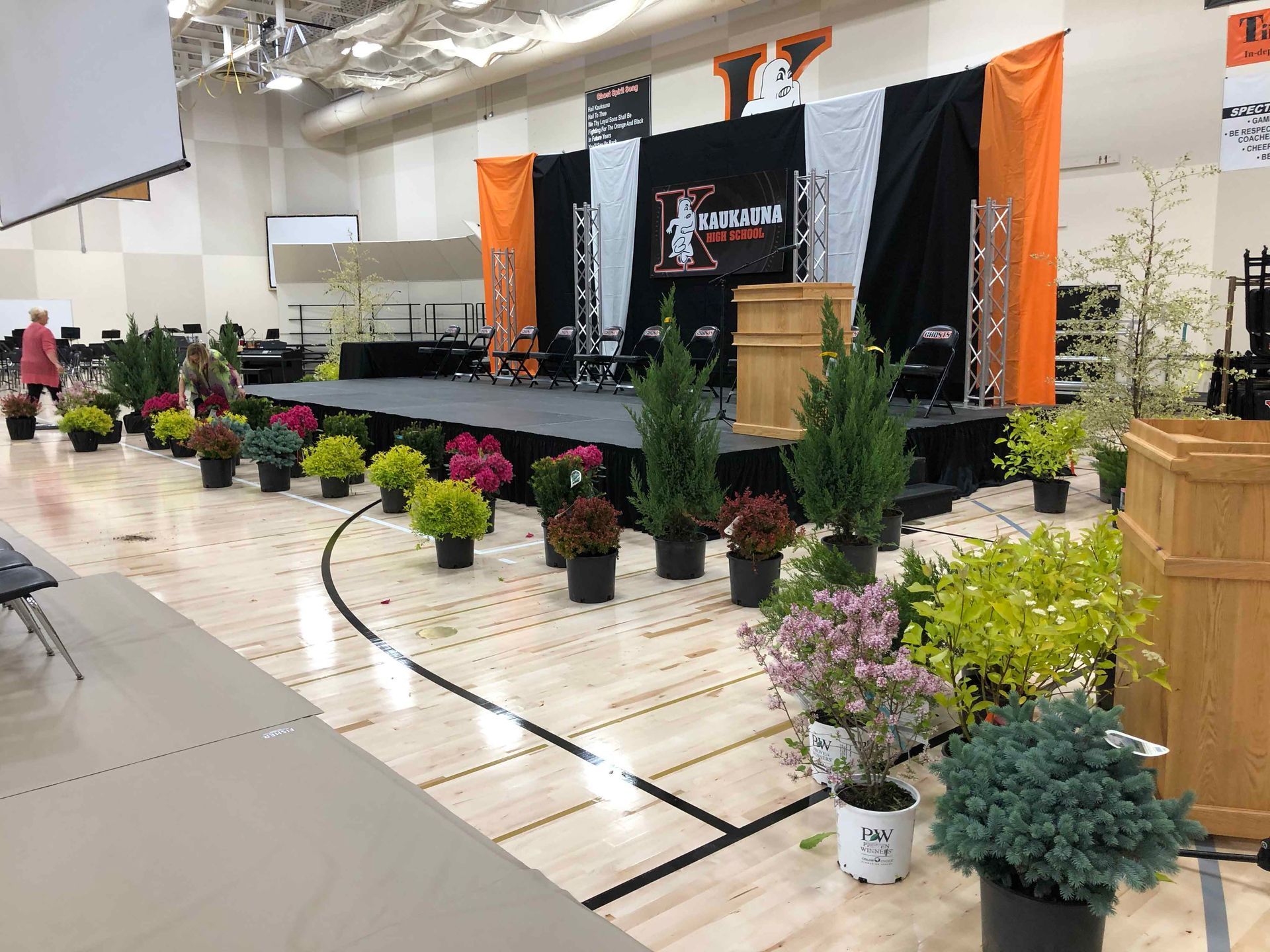 A stage with potted plants and a podium in a gym.