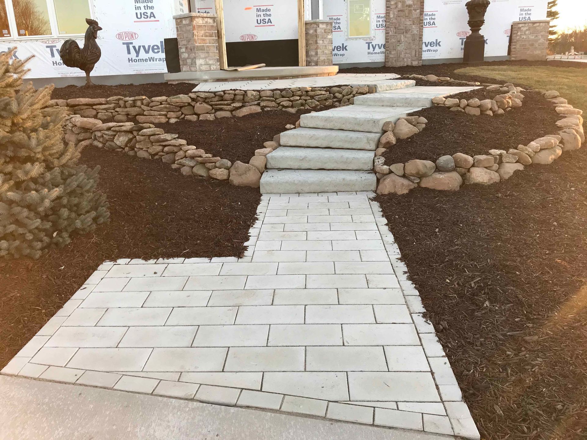 A rooster is standing on a brick walkway in front of a house under construction.