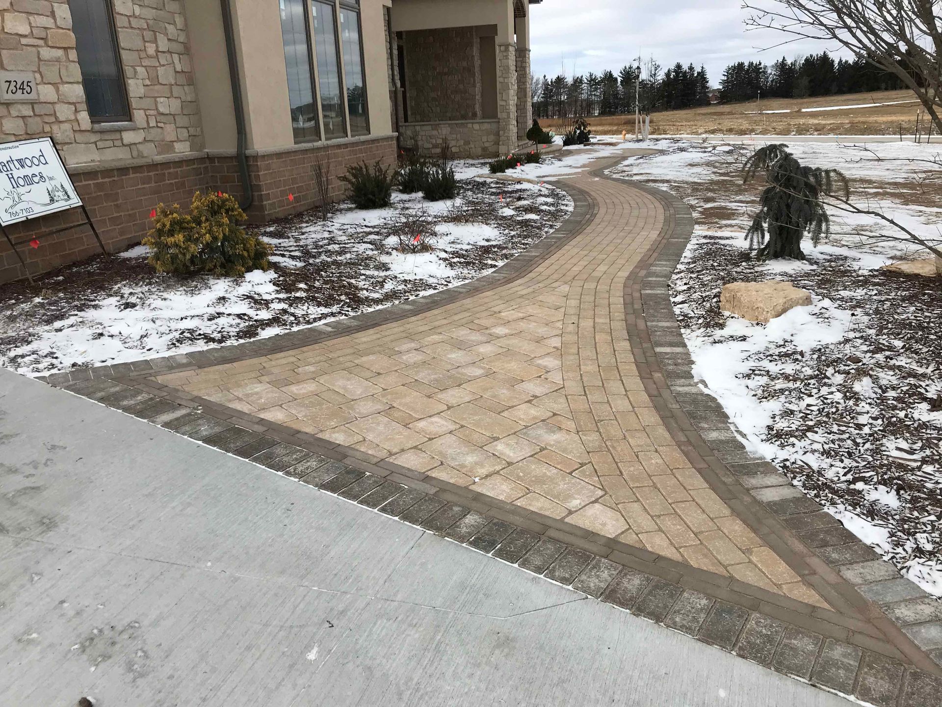 A brick walkway leading to a house with snow on the ground.