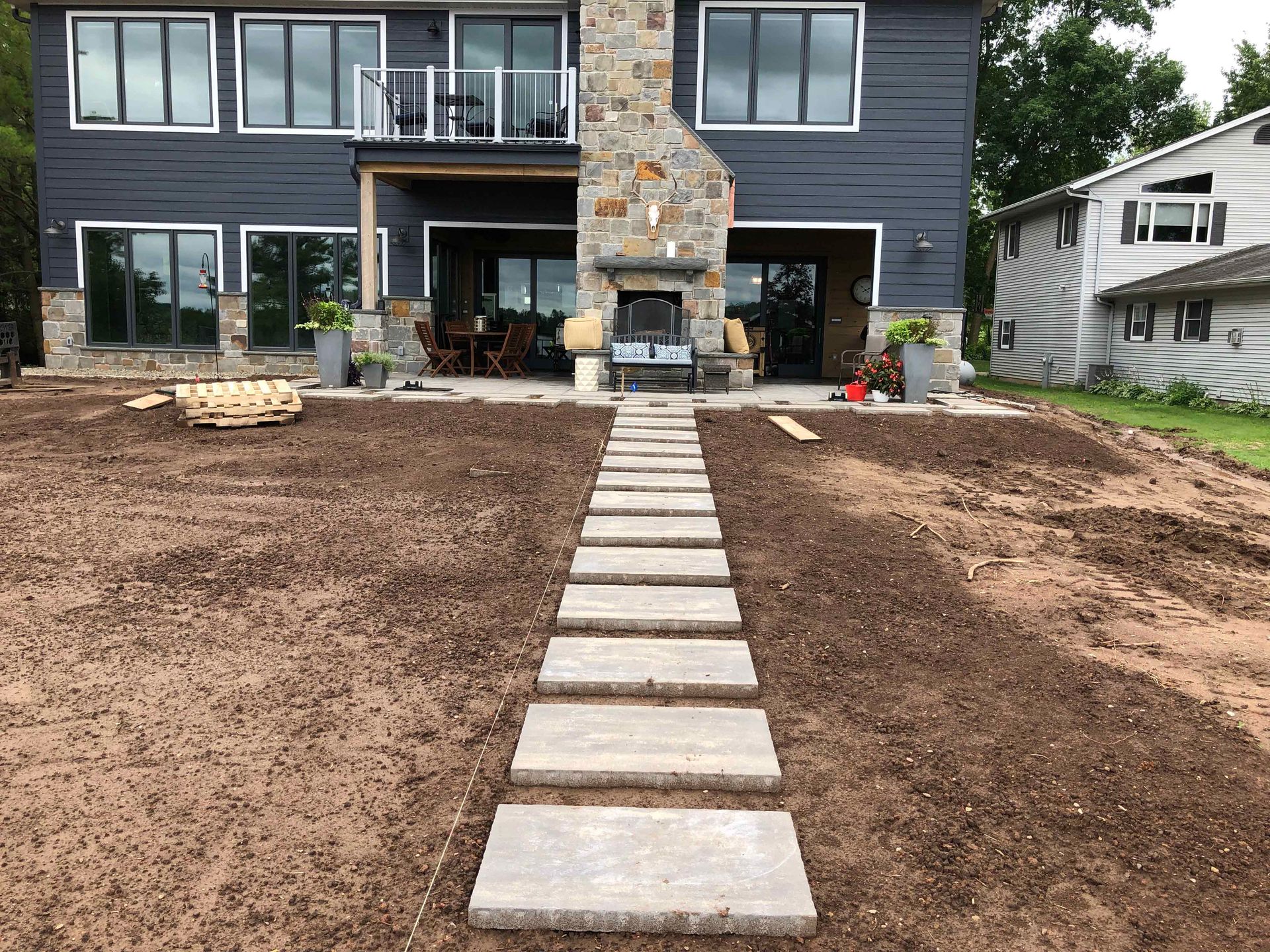 A stone walkway leading to a large house with a fireplace in the backyard.