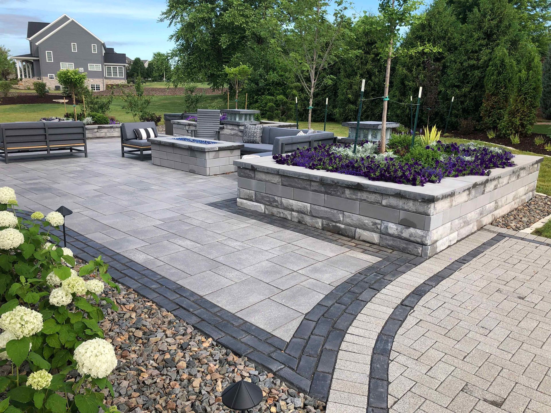 A patio with a fire pit , flowers , and a bench.