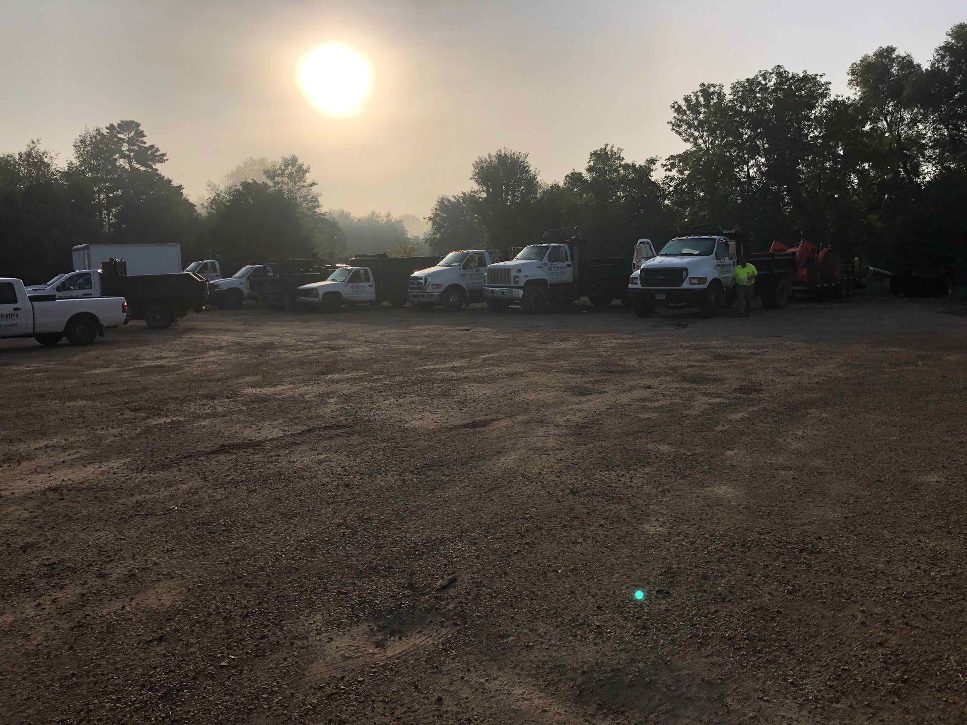 A row of trucks are parked in a gravel lot.