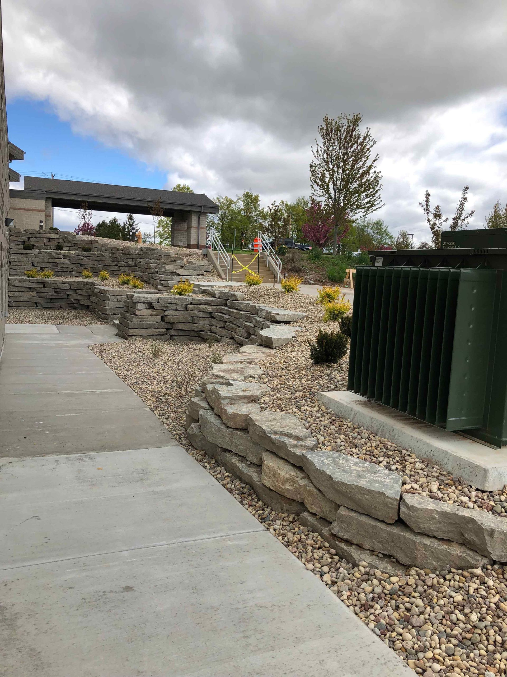 A stone wall is surrounded by gravel and a concrete walkway.