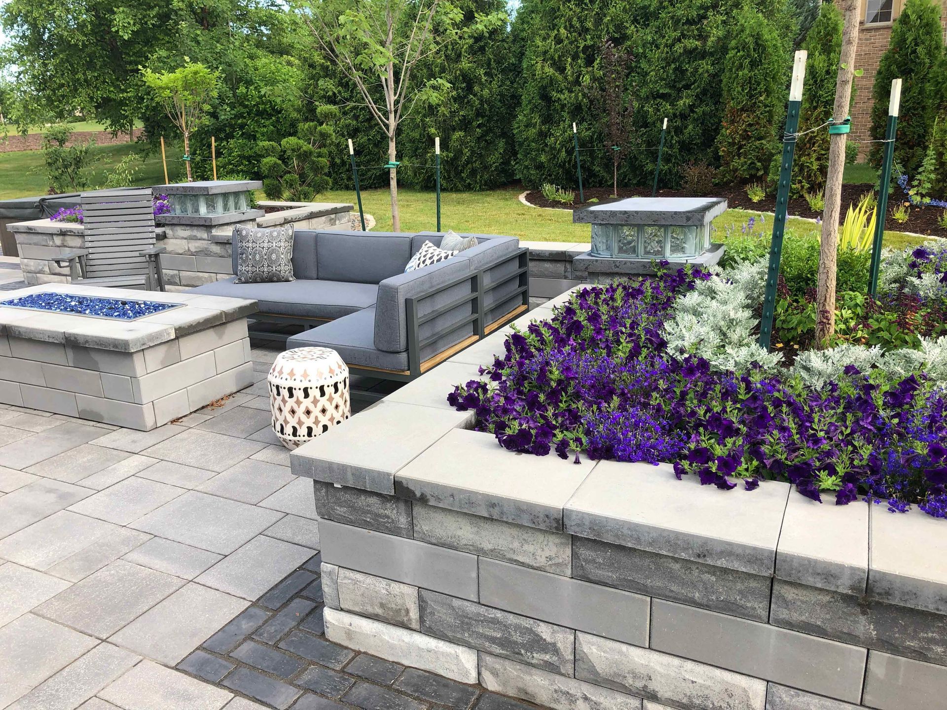 A patio with a fire pit , couch , and purple flowers.