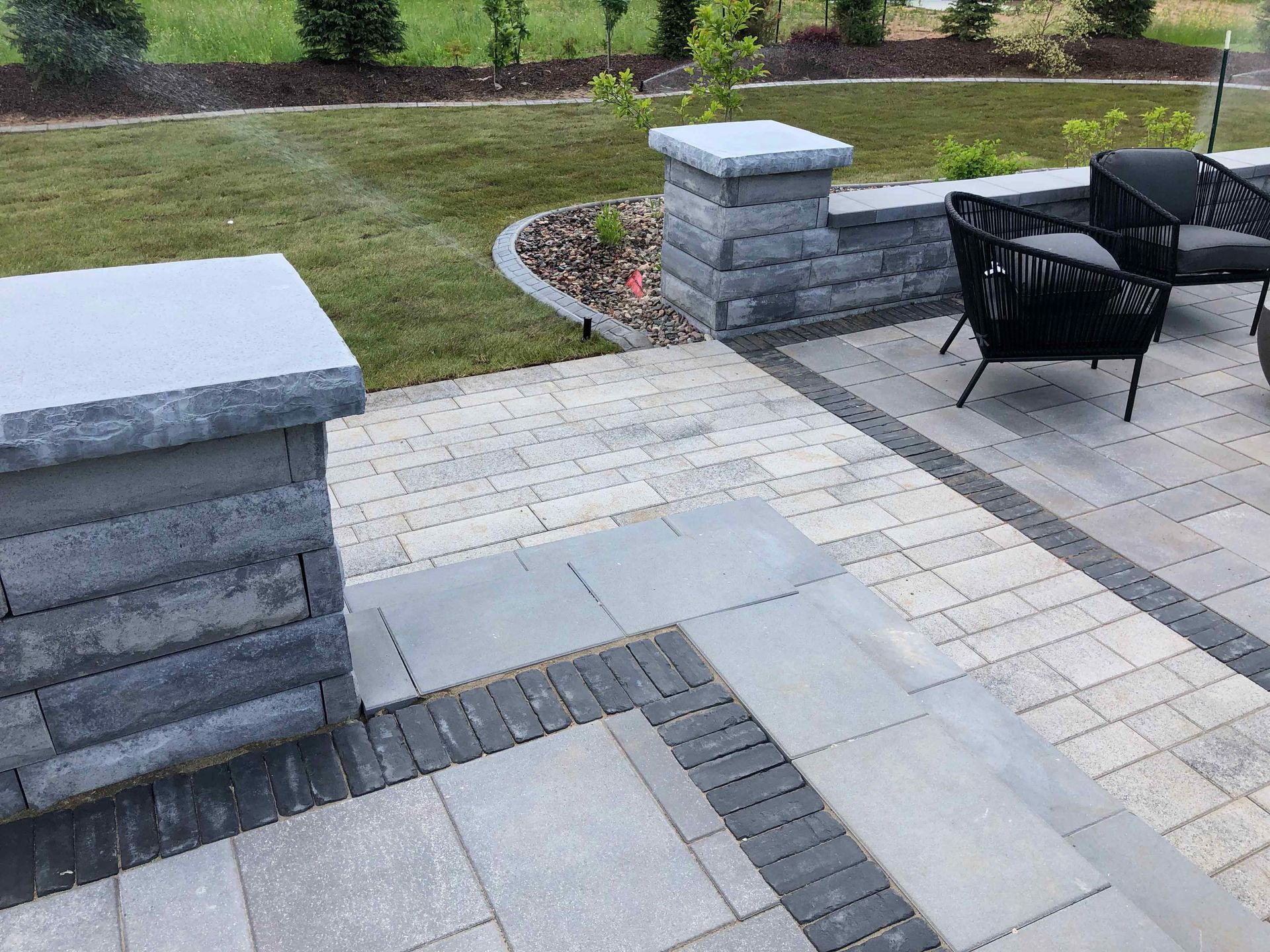 A patio with a brick wall , chairs and a table.
