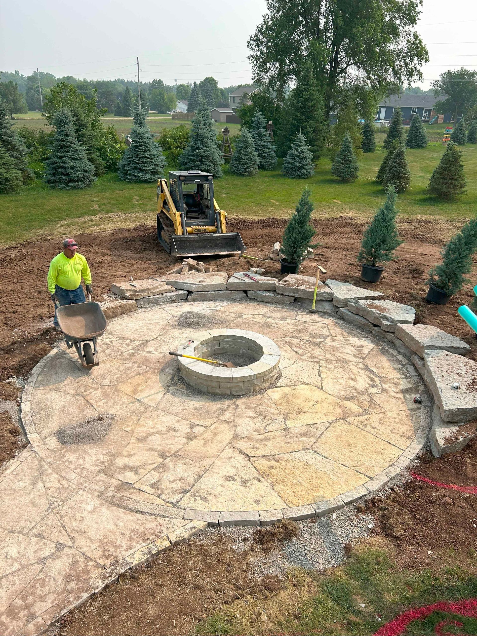 A man is pushing a wheelbarrow in front of a fire pit.