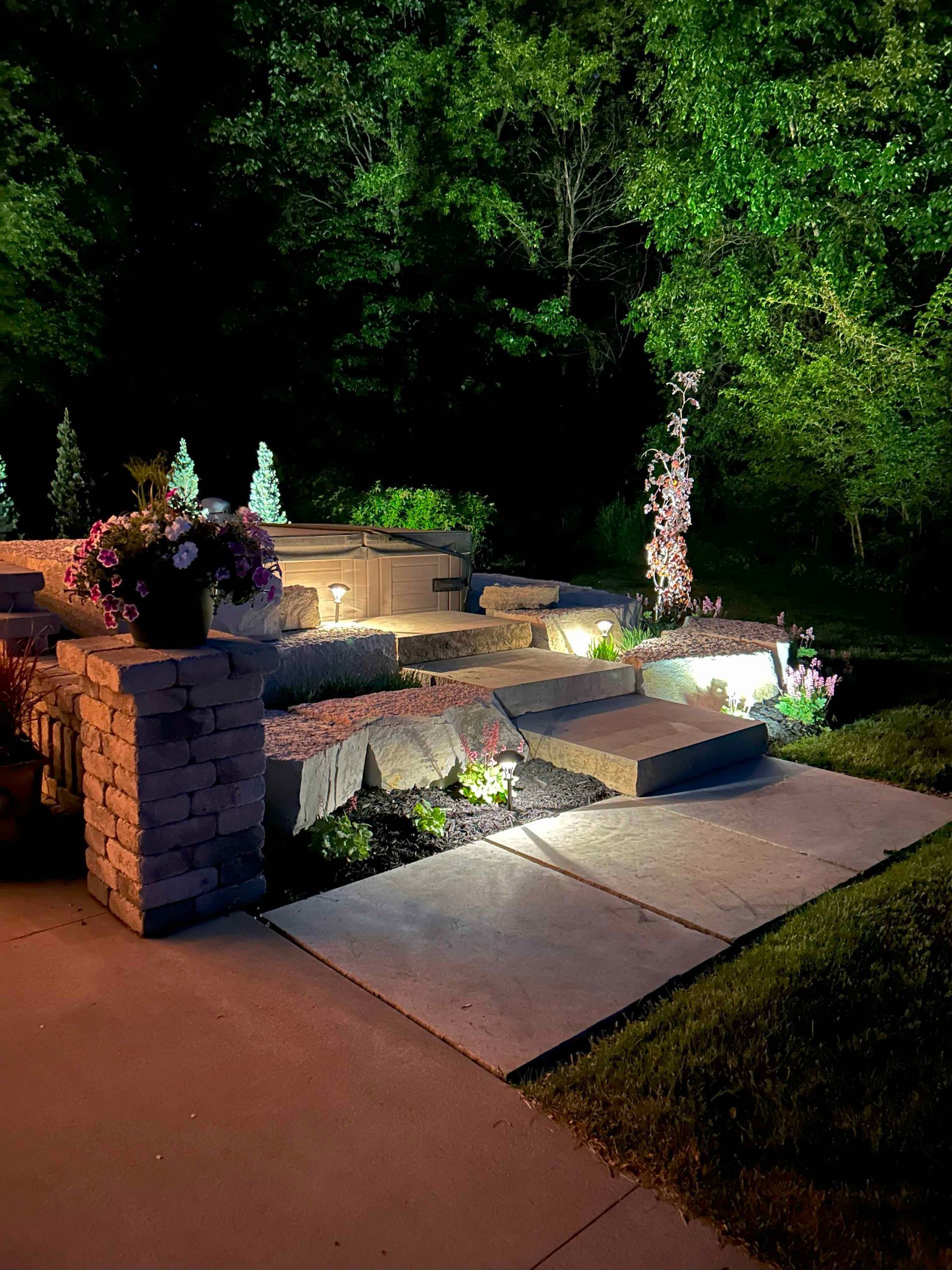 A walkway with stairs and flowers is lit up at night.