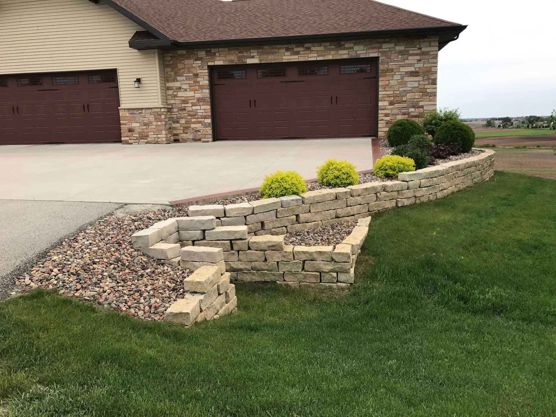 A house with two garage doors and a stone wall in front of it.