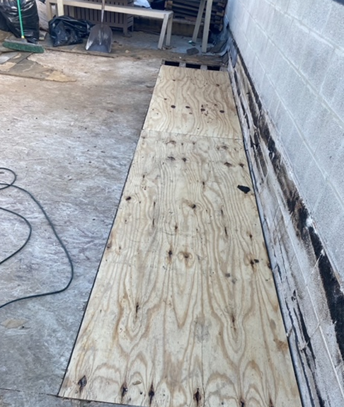 a piece of plywood is sitting on the ground next to a brick wall