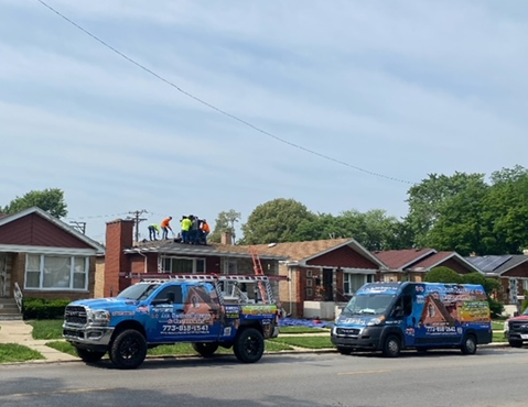 two trucks are parked in front of a house with workers on the roof