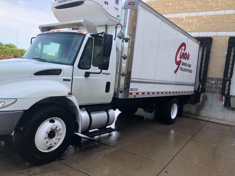 A white refrigerated truck is parked in front of a building.