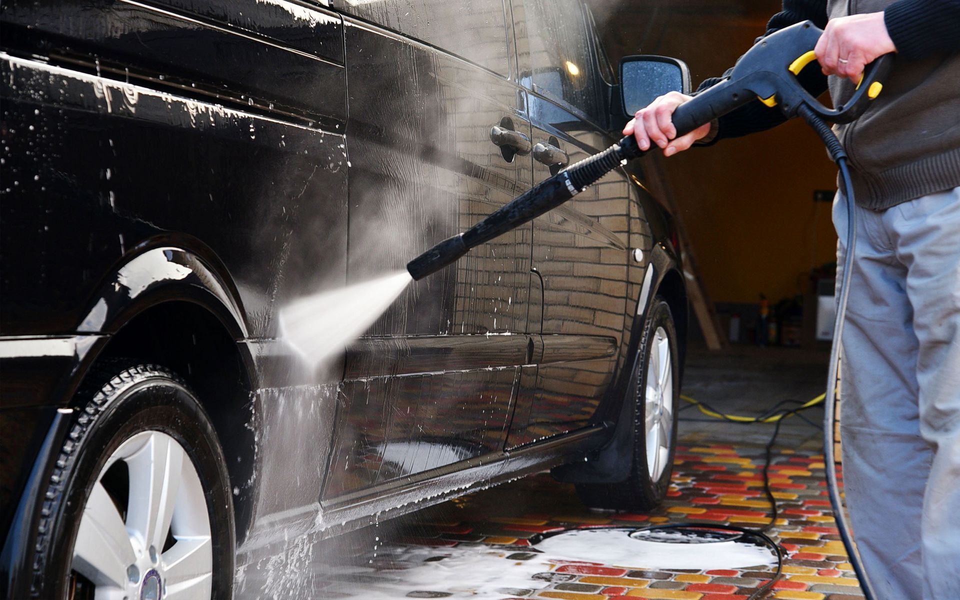 A man is washing a black van with a high pressure washer.