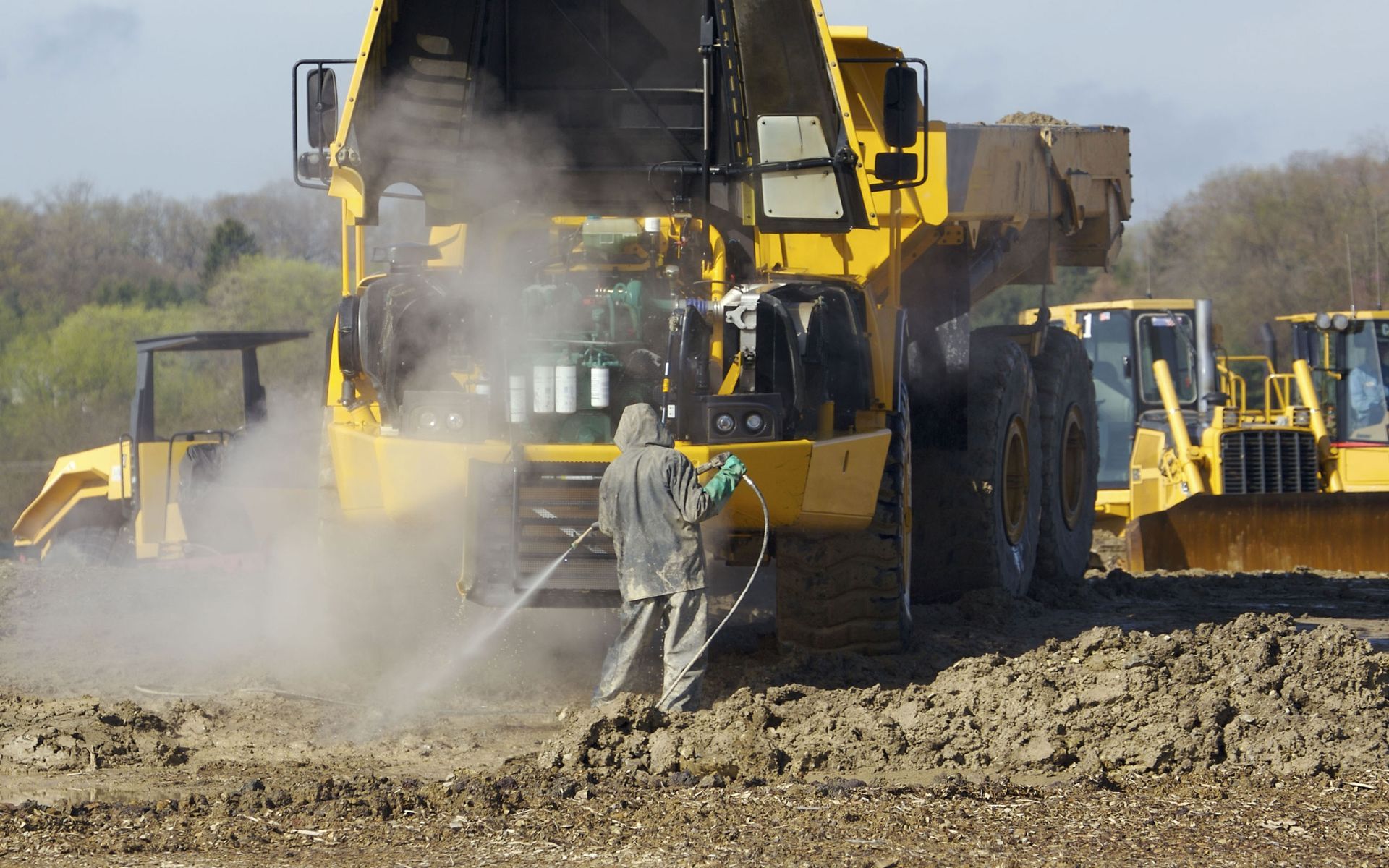 A man is spraying a yellow dump truck with a hose.