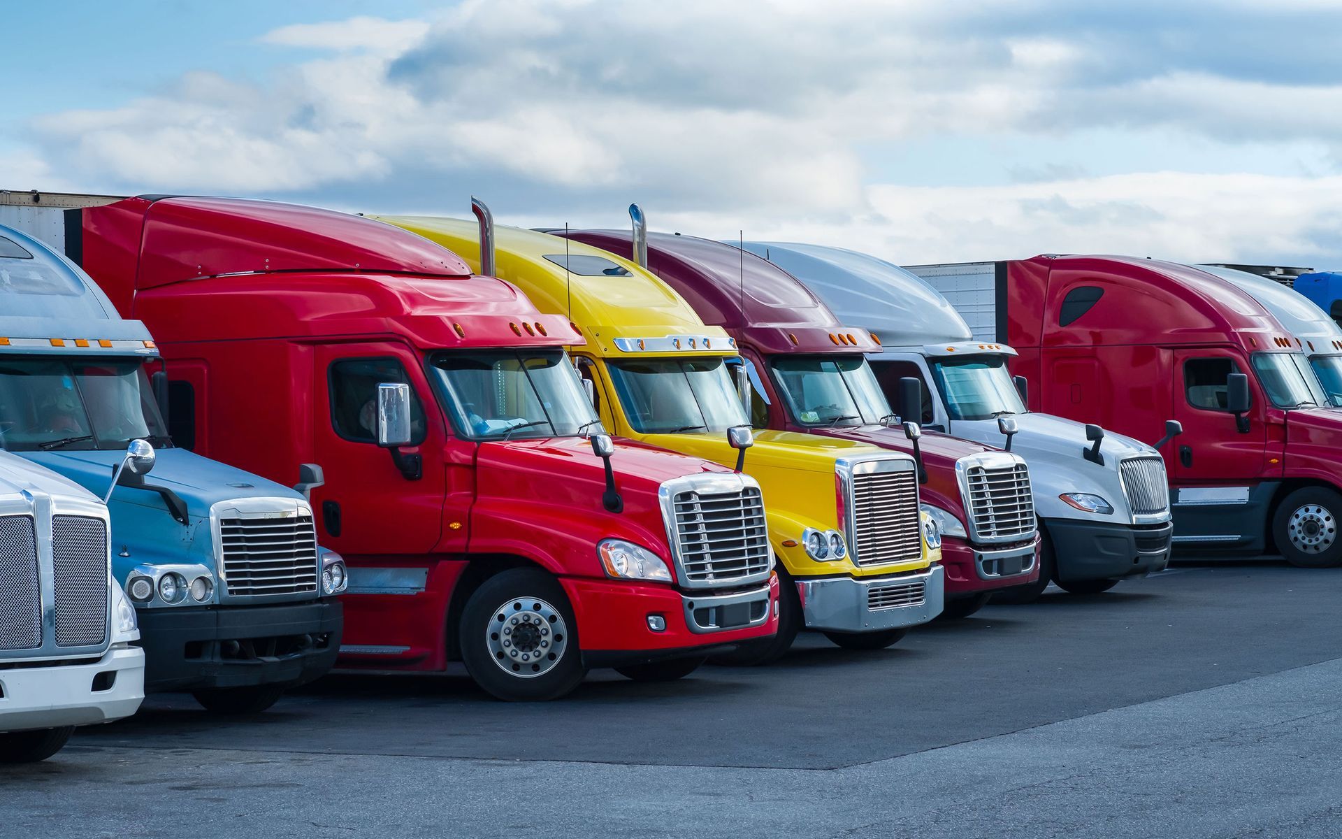 A row of semi trucks parked next to each other in a parking lot.