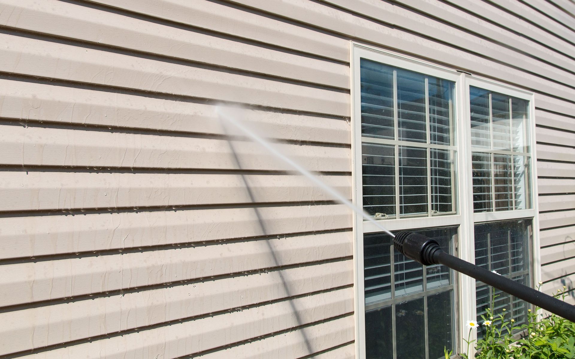 A person is cleaning the side of a house with a high pressure washer.